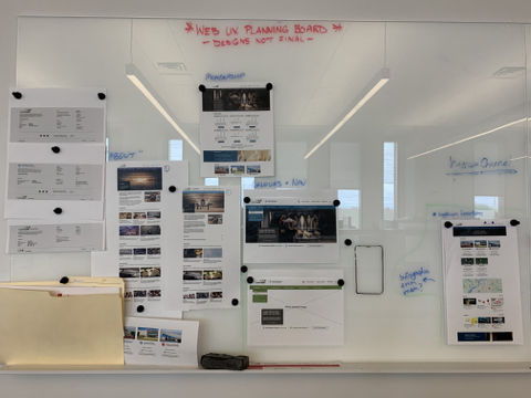 A whiteboard affixed with several pieces of paper that have been printed with indistinguishable text and images.